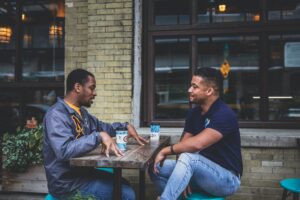 Two black men sit at a table outside 