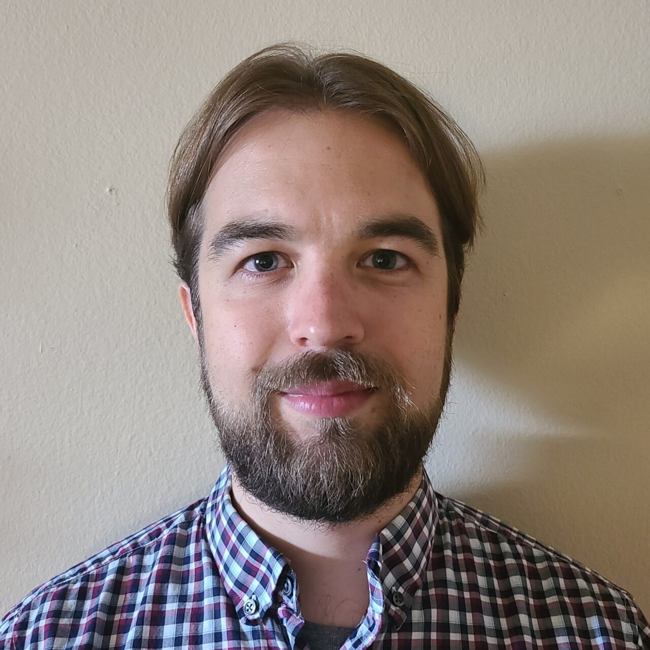 Photo of man in plaid shirt standing against white wall