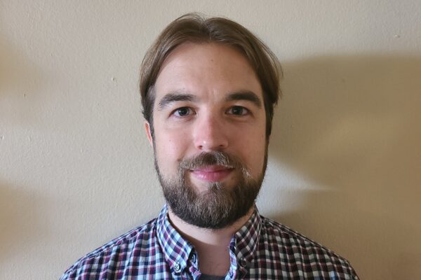 Photo of man in plaid shirt standing against white wall