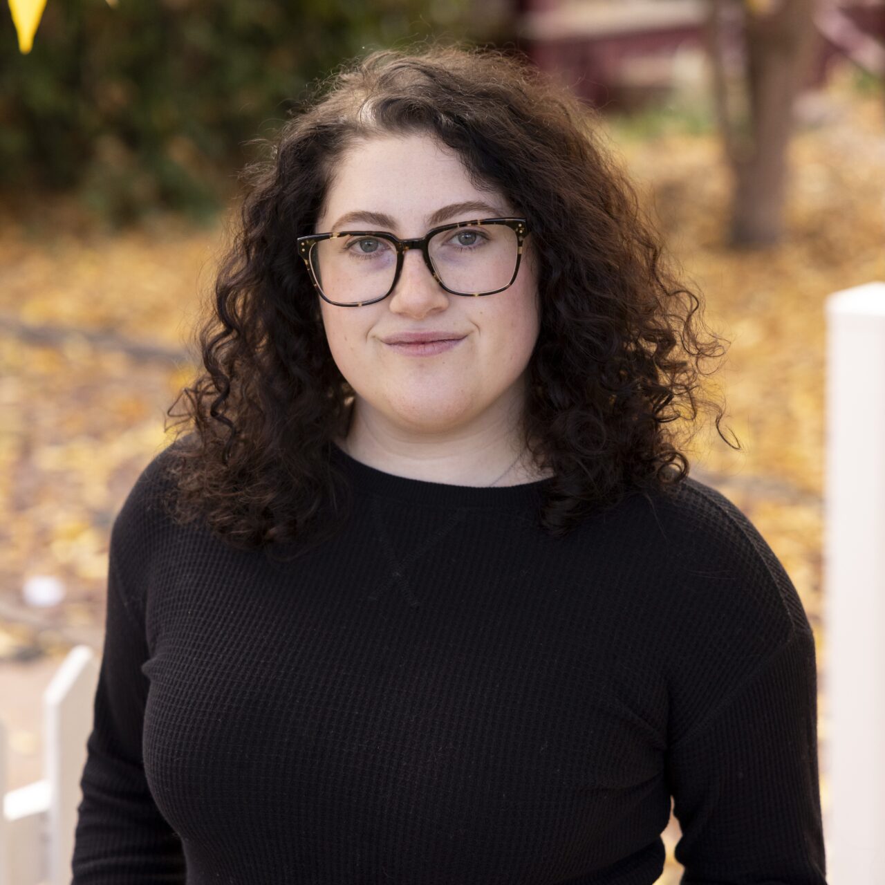 Woman with brown, curly hair poses in a Fall scene