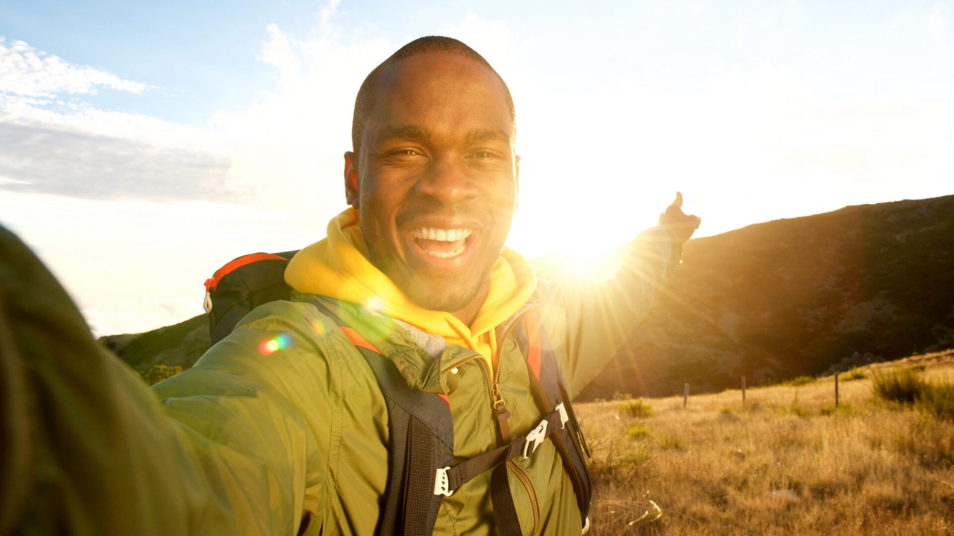 A man points backwards towards a mountain and the setting sun
